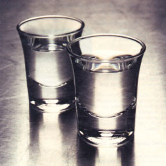 Two glasses of clear spirits on a shiny metallic surface